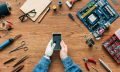 cropped image of  electronic engineer with prosthetic arm using smartphone at table surrounded by